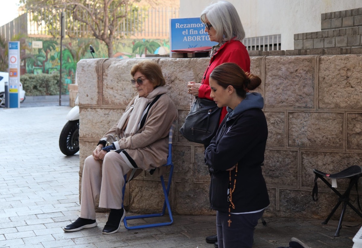 Lourdes Varela reza de rodillas en una vigilia junto a una voluntaria - marzo 2023